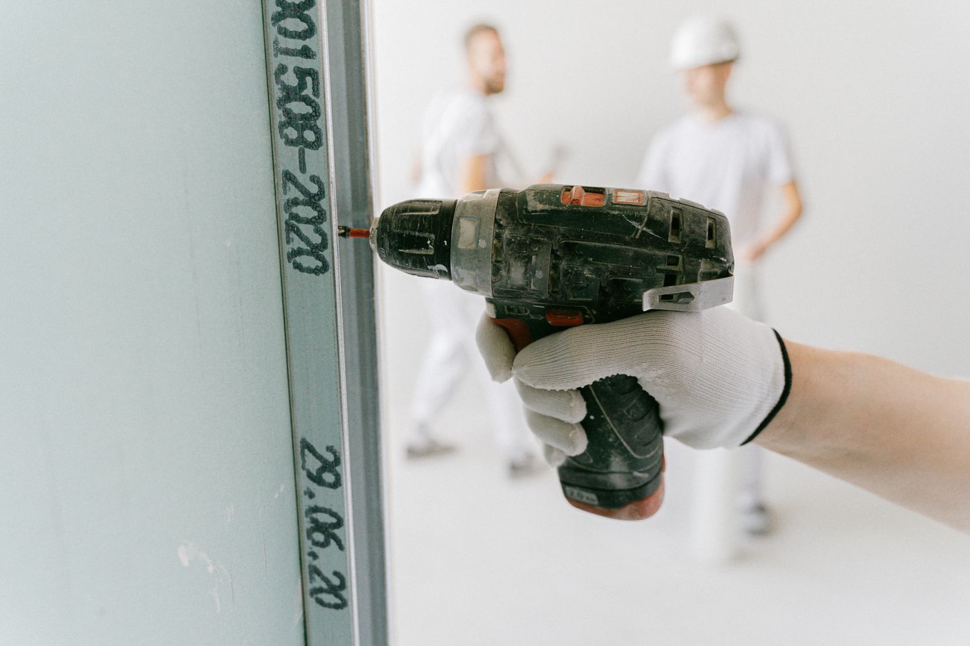 Hand met een boormachine bij een metalen profiel tegen een wand